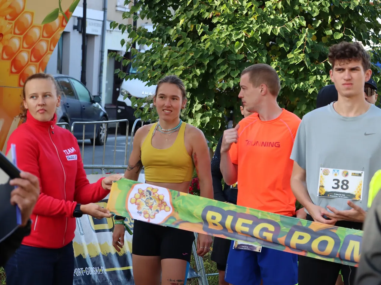 Zawodnicy biegu na 7 km za taśmą startową z napisem Bieg po Miód