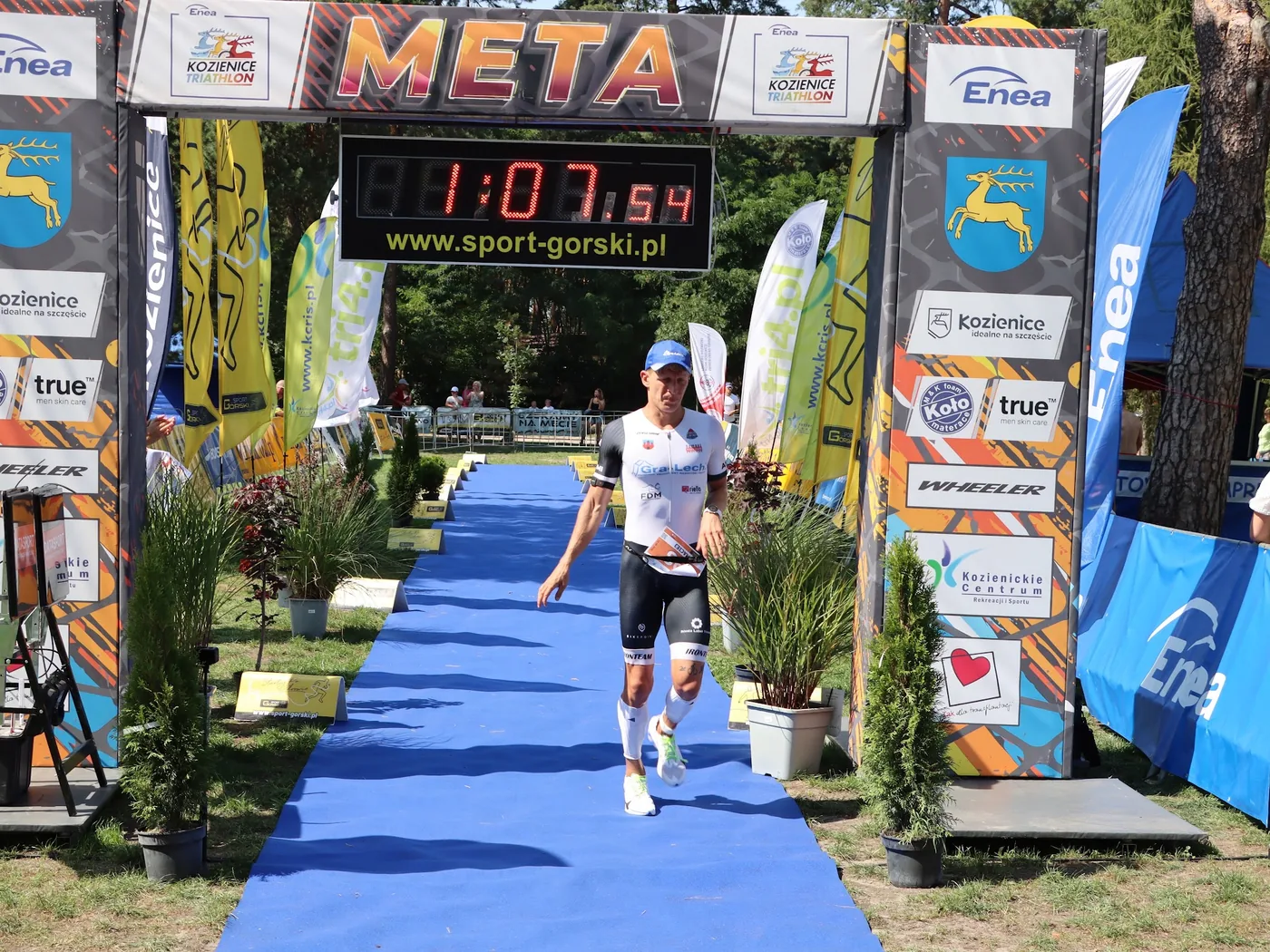 Zawodnik wbiegający na metę ENEA Kozienice Triathlon 2026 pod bramą z zegarem